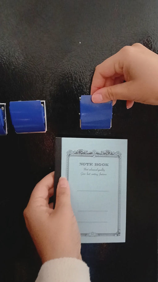 PLUS Extra Strong Magnet Clip holding a notebook on a fridge